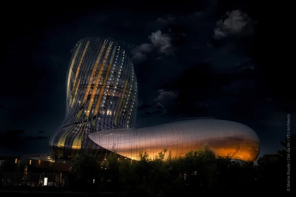 Vue nocturne de la Cité du Vin à Bordeaux, façade illuminée.