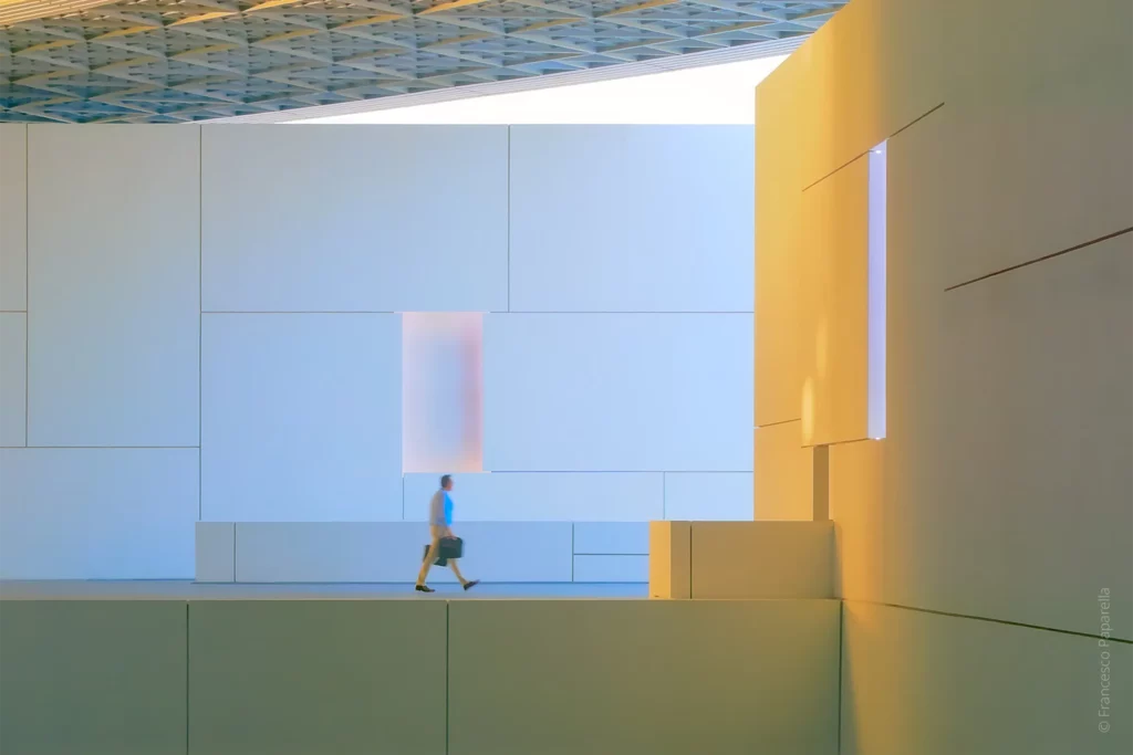 Extérieur du Louvre Abu Dhabi, sous la coupole ajourée laissant passer la lumière naturelle, avec un passant en mouvement. Projet lumière conçu par 8’18’’ avec la participation de David Roger pendant 7 ans, des études à la phase chantier.